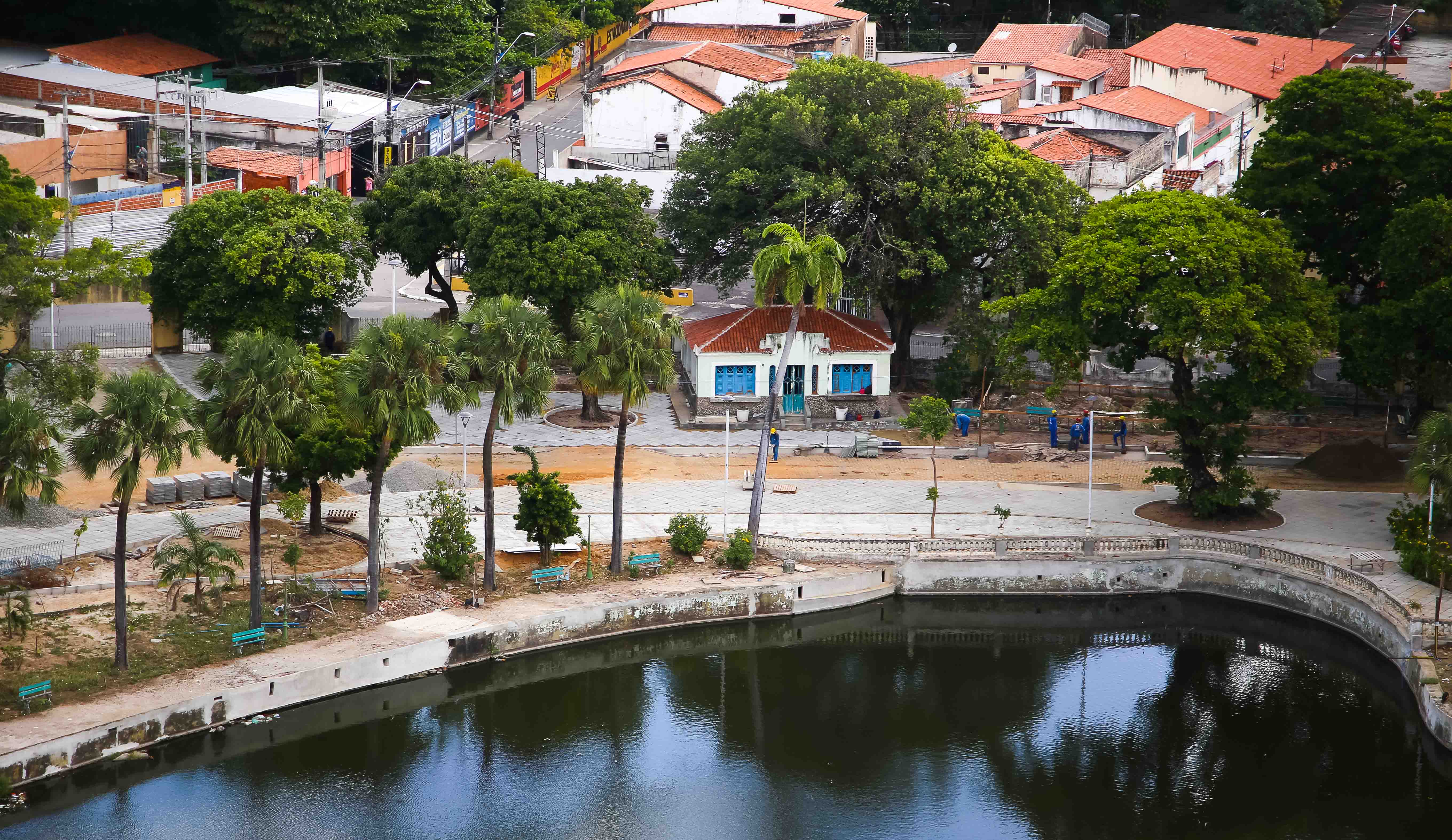 imagem com vista aérea de lago com árvores ao redor e casas ao fundo e operários trabalhando 